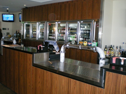 Timber-clad bar with stainless work surfaces and glass-door fridges
