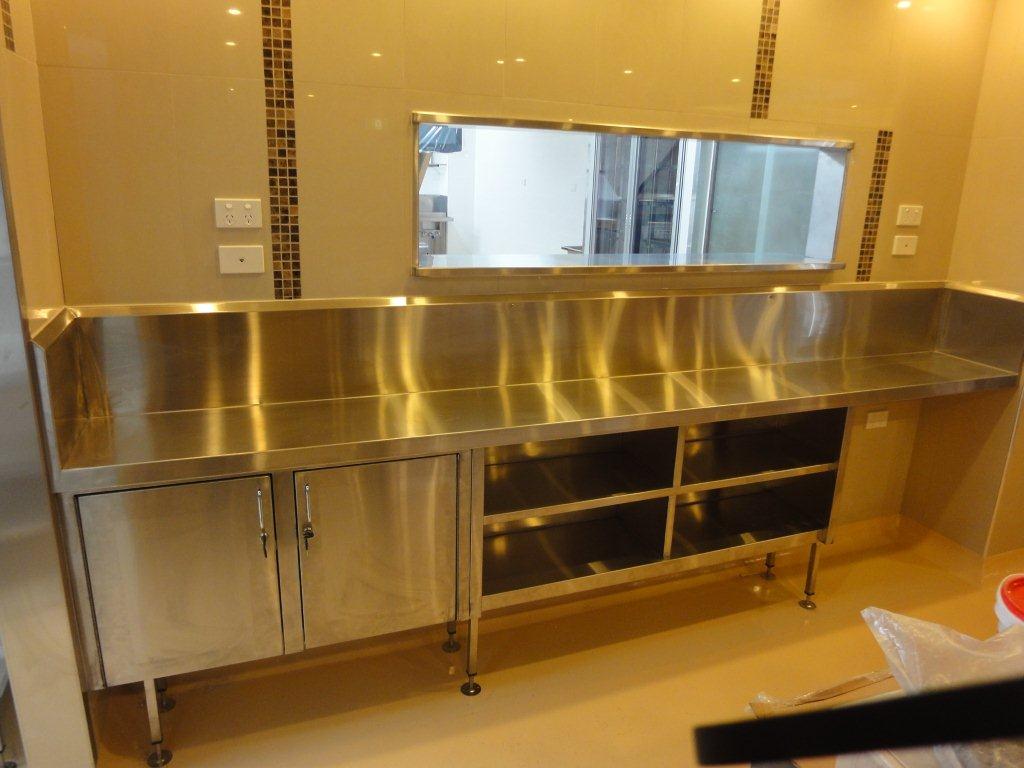 Long stainless steel servery bench with cupboards under a pass-through window