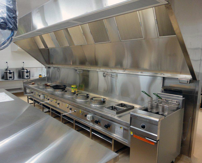 Stainless canopy hood over a full cooking line with wok burners and a fryer